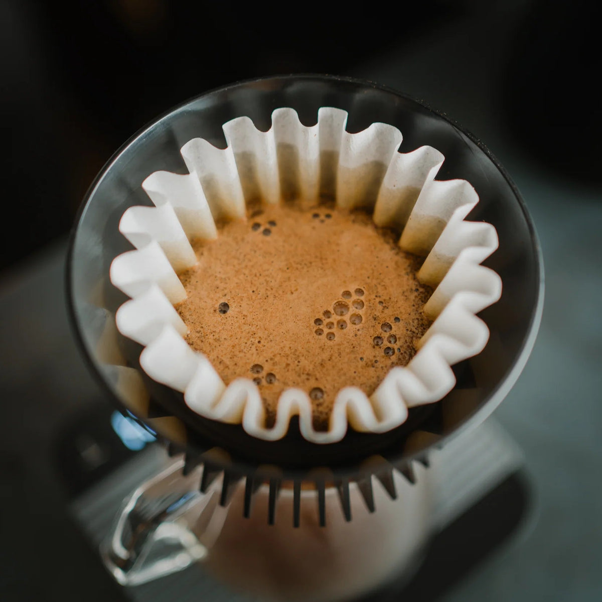 Coffee filter with coffee grounds in a glass carafe on a dark surface