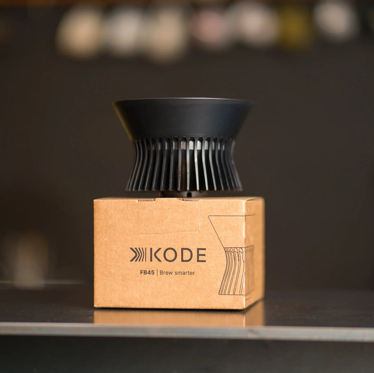 Matte black Kode FB45 pour-over coffee dripper resting on its branded kraft cardboard packaging box